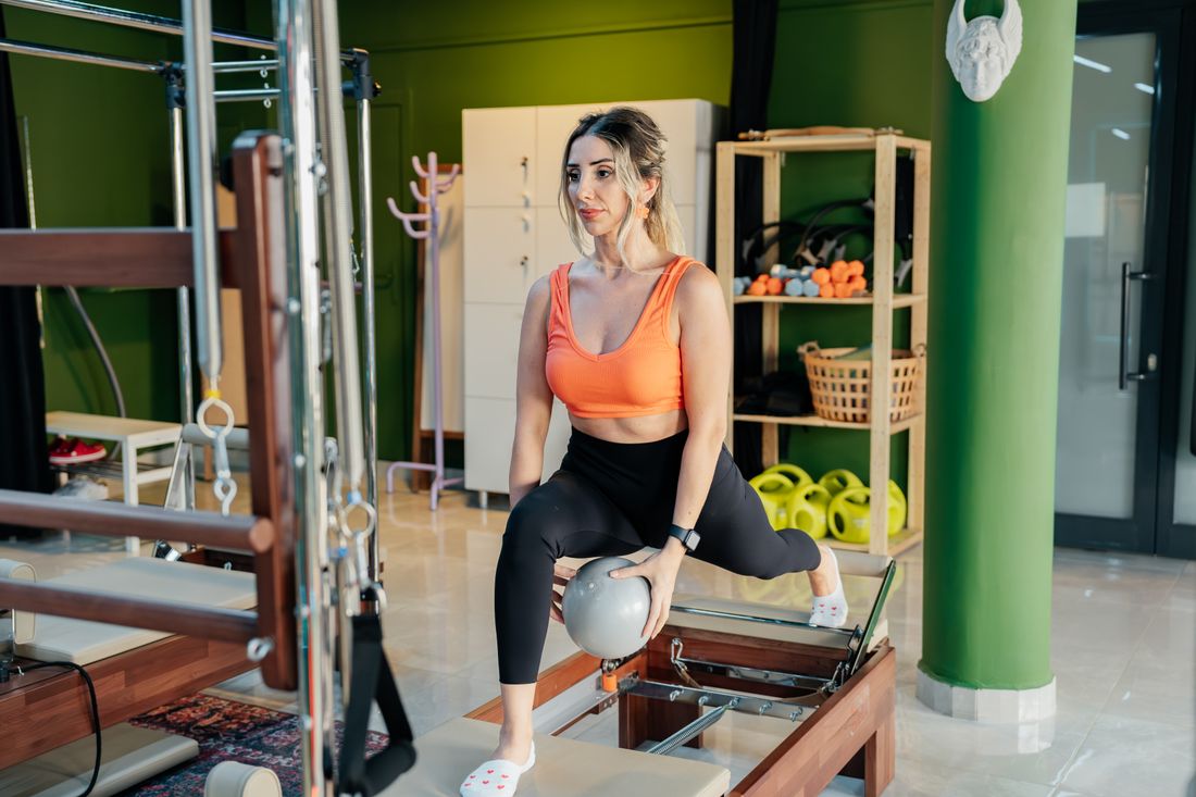 Mulher praticando pilates no reformer, realizando um movimento sobre a máquina